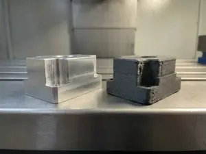 CNC-gefrästes Aluminiumteil neben einem 3D-gedruckten Prototyp gleicher Geometrie auf einer Stahlwerkbank.