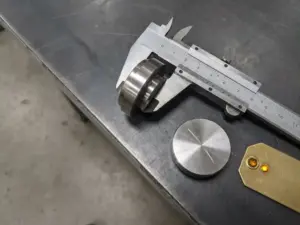 Präzisionsgefertigtes Metallteil in Messschieber eingespannt, daneben abgelehntes Bauteil mit Kratzer, CNC-Fertigungsumgebung.