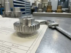 Präzisionsgefertigtes Metallteil auf technischer Zeichnung mit Messschieber auf grauer Werkstattoberfläche.